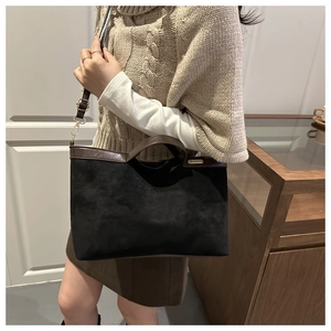 Detail of black suede tote bag with brown leather handles and gold brand plaque