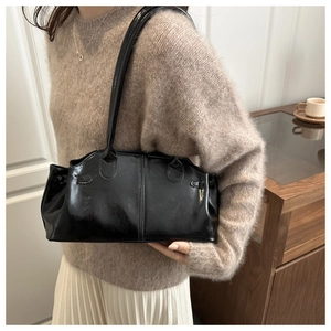 Dettaglio di una borsa a spalla nera lucida con cuciture e spalline sottili