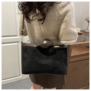 Detail of black suede tote bag with leather straps and gold logo on a model