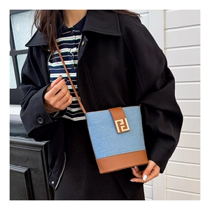 Detail of blue denim and brown leather bucket bag with a golden geometric metal buckle