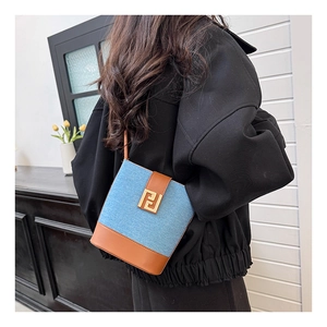 Detail of blue denim bucket bag with brown leather trim and gold geometric buckle