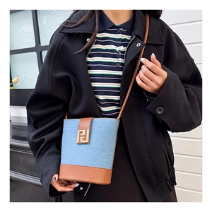 Detail of denim and leather bucket bag featuring a gold metal buckle and crossbody strap