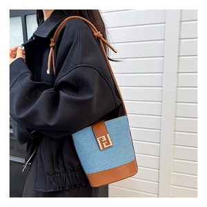 Close-up of denim bucket bag with leather trim and gold hardware on model shoulder