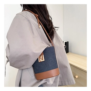 Detailed shot of a navy denim bucket bag with brown leather base and gold metal hardware