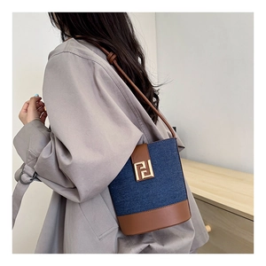 Detail of denim bucket bag with brown leather trim and golden metal logo on grey coat