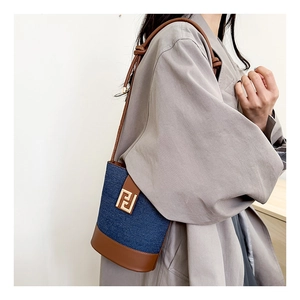 Detail of denim bucket bag showing brown leather trim and golden geometric logo buckle