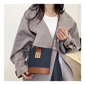 Detail of denim and brown leather bucket bag with gold geometric metal clasp
