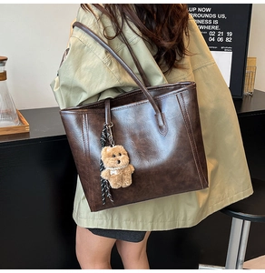 Detail of dark brown leather tote bag with plush bear charm and vintage texture