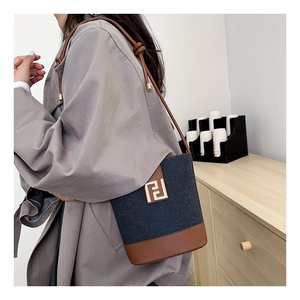Detailed view of the blue fabric and brown leather bucket bag with golden hardware