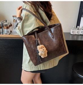 Detail of a large vintage oil wax leather tote bag in dark brown with a bear charm