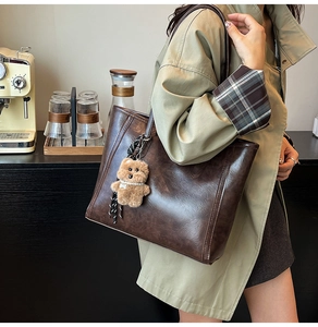 Detail of dark brown leather tote bag with plush bear charm in a cafe setting
