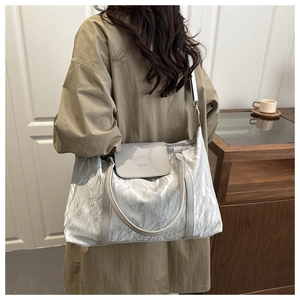 Detail of silver metallic tote bag with wrinkled texture and light gray leather handle