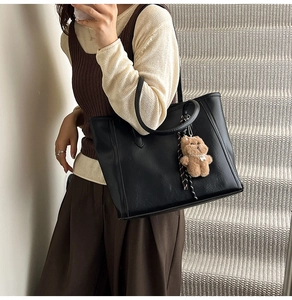 Detail of black faux leather tote bag with long straps and brown plush bear charm