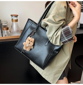 Detail of black PU leather tote bag texture with cute brown teddy bear pendant charm