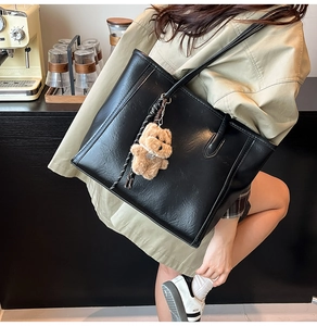 Close-up of black retro tote bag with natural leather texture and plush puppy charm