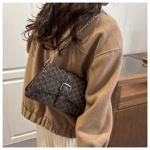Detail of vintage brown chain bag with letter print worn on shoulder with casual outfit