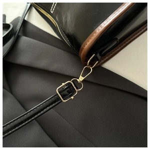 Gros plan d'un sac en cuir PU brillant noir avec boucle dorée et bords marron finis