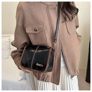 Détail d'un petit sac bandoulière noir avec coutures blanches et logo doré sur mannequin