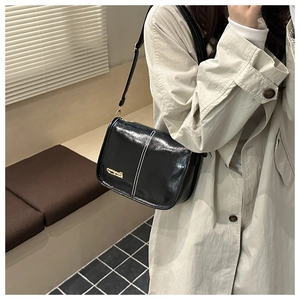Detailed view of black glossy shoulder bag with gold metal plaque and white stitching