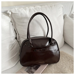Detailed view of dark brown glossy patent leather shoulder bag with bow and gold logo