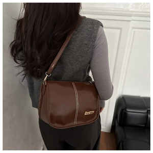 Détail d'un sac à bandoulière marron brillant avec surpiqûres blanches et logo doré