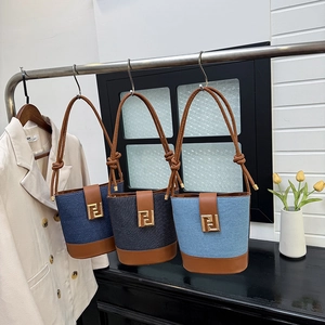 Three trendy denim bucket bags with leather trim hanging on a rack in a boutique setting