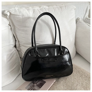 Detail of black bow accent and gold lettering on a chic leather pillow shoulder bag