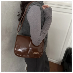 Détail du sac bandoulière vintage en cuir verni marron avec surpiqûres et logo doré