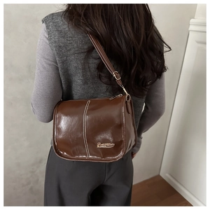 Detail of a brown glossy PU leather crossbody bag featuring white contrast stitching and logo