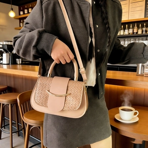 Détail du sac bandoulière rose nude avec texture tressée et boucle dorée dans un café chaleureux