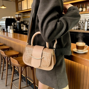 Détail du rabat tressé et boucle dorée sur un sac bandoulière beige dans un café