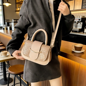 Detail of beige woven leather crossbody bag with gold hardware in a cafe setting
