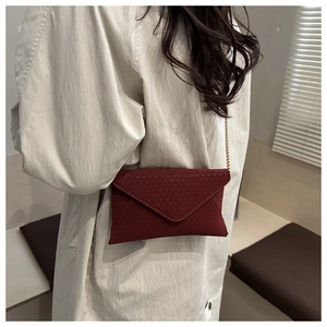 Detail of burgundy envelope bag with gold chain strap and geometric embossed texture