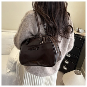 Close-up of a dark brown patent leather shoulder bag featuring a decorative bow detail