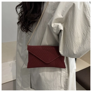 Close-up of burgundy V-quilted envelope bag with gold chain strap on a trench coat