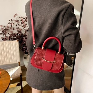 Détail du sac à main rouge tissé avec boucle dorée en croissant et poignée dans un décor cosy