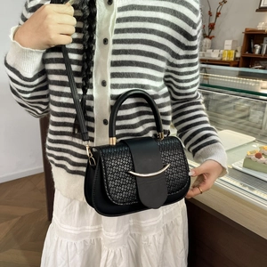 Détail du sac bandoulière noir tressé avec boucle dorée porté par un mannequin