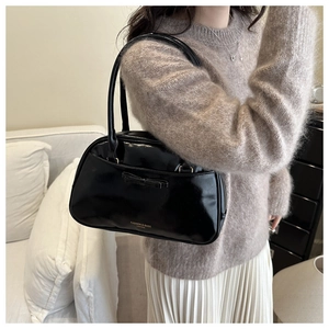 Close-up of black patent leather hobo bag with bow detail and gold lettering