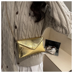 Detail of gold envelope bag with ripple texture and elegant metal chain strap for women