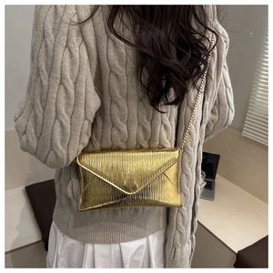 Detail of golden envelope bag with wavy texture and metallic chain strap on a shoulder