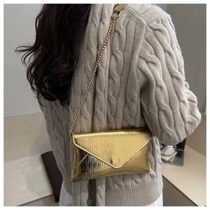 Close-up of golden envelope chain bag with vertical texture worn on a beige sweater