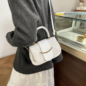 Détail du sac selle blanc tissé avec une boucle métallique dorée sur le rabat avant
