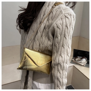 Detail of a gold metallic envelope bag with vertical texture and fine chain strap