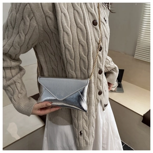 Detail of silver metallic envelope bag with ripple texture and gold chain on model