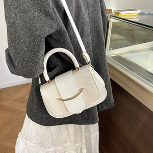 Détail du sac à main blanc à texture tressée et boucle dorée dans un cadre épuré