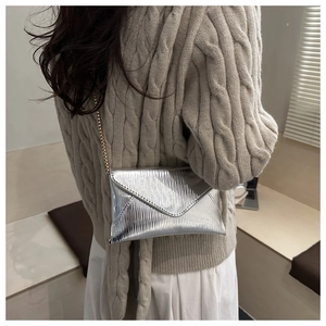 Detail of silver metallic envelope crossbody bag with fine wavy texture and gold chain