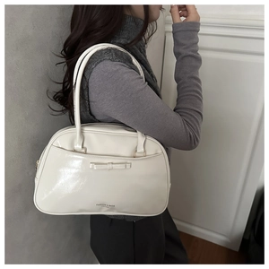 Close-up of cream glossy leather pillow bag featuring a bow detail and side profile view