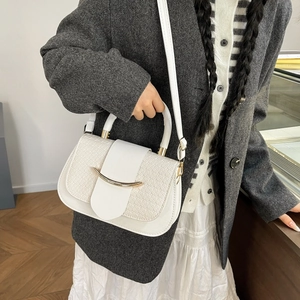 Détail du sac à bandoulière blanc à boucle dorée porté par un mannequin en costume gris
