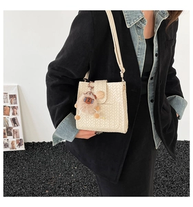 Detail of cream woven shoulder bag featuring a wooden buckle and plush charm accessory