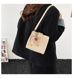 Detail of beige woven crossbody bag with wood-grain buckle and brown plush bear charm